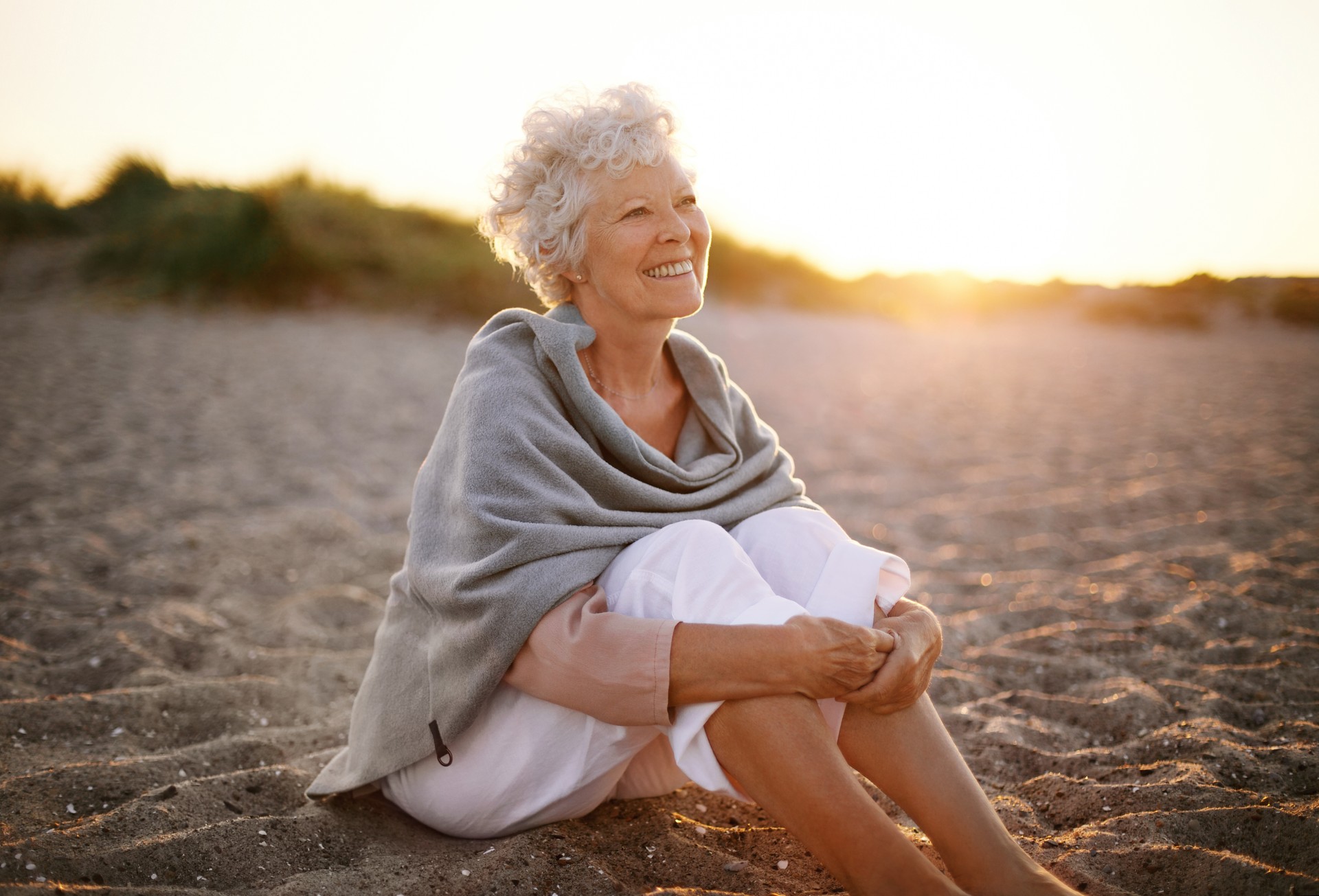 Cheerful old woman sitting on the beach after having hypnosis